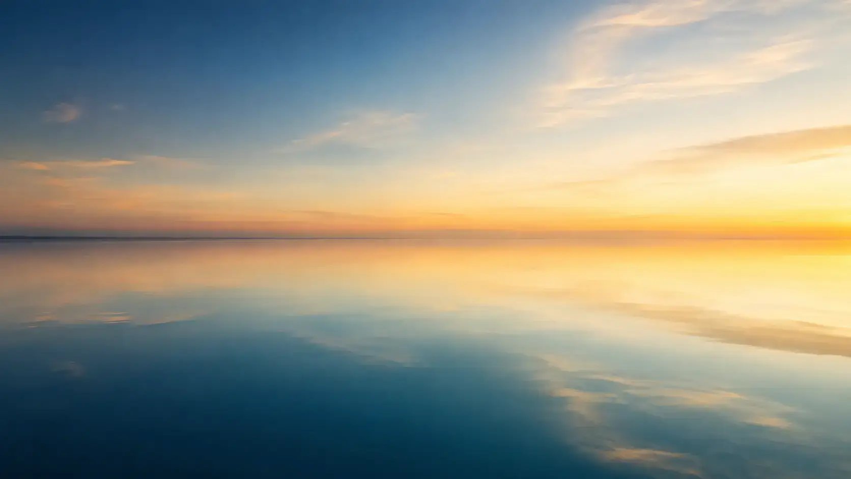 Still water holding a soft, calm reflection of open sky at dawn, in muted navy, teal, and gold tones