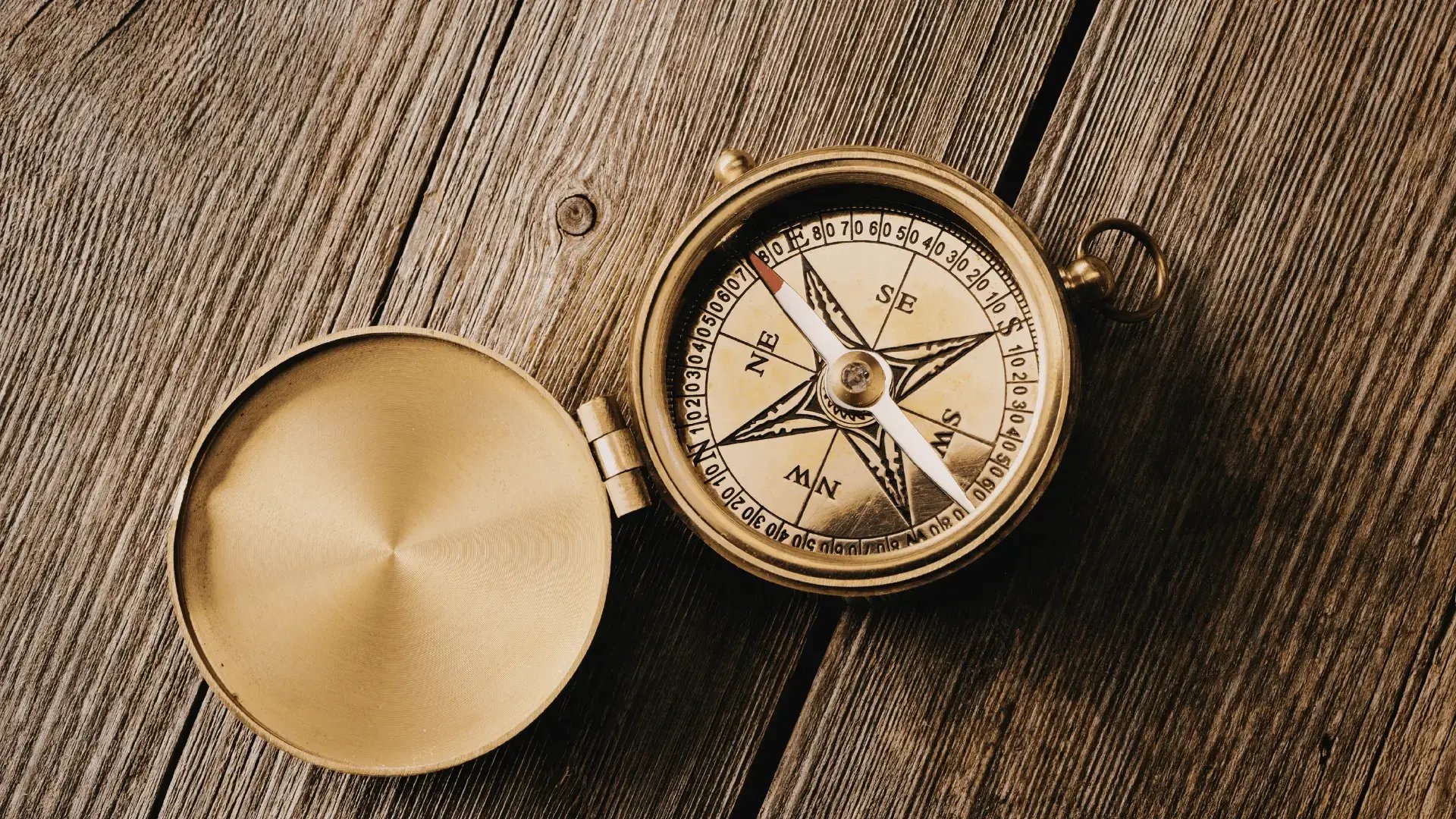 Vintage brass compass with its lid open, resting on a weathered wooden surface Trauma Therapist Institute