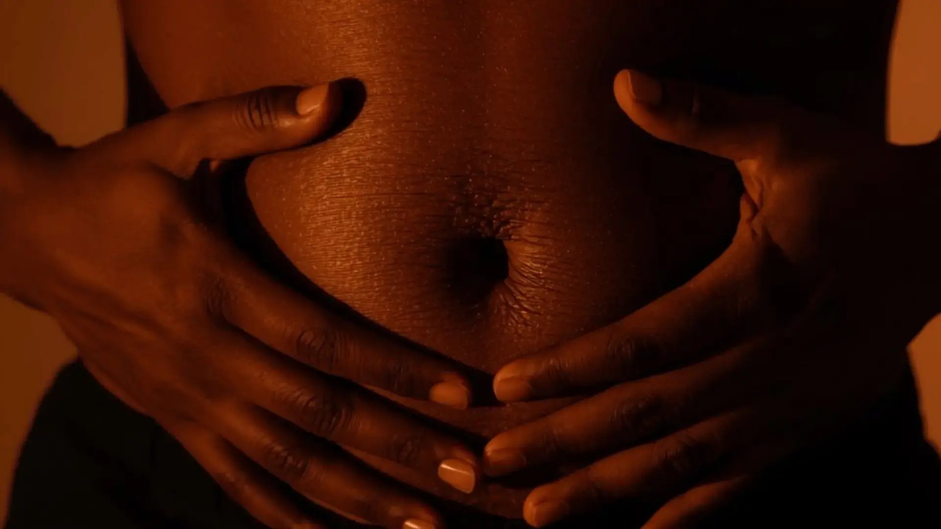 Close-up of hands resting on the belly in a diaphragmatic breathing position, in warm amber light Trauma Therapist Institute