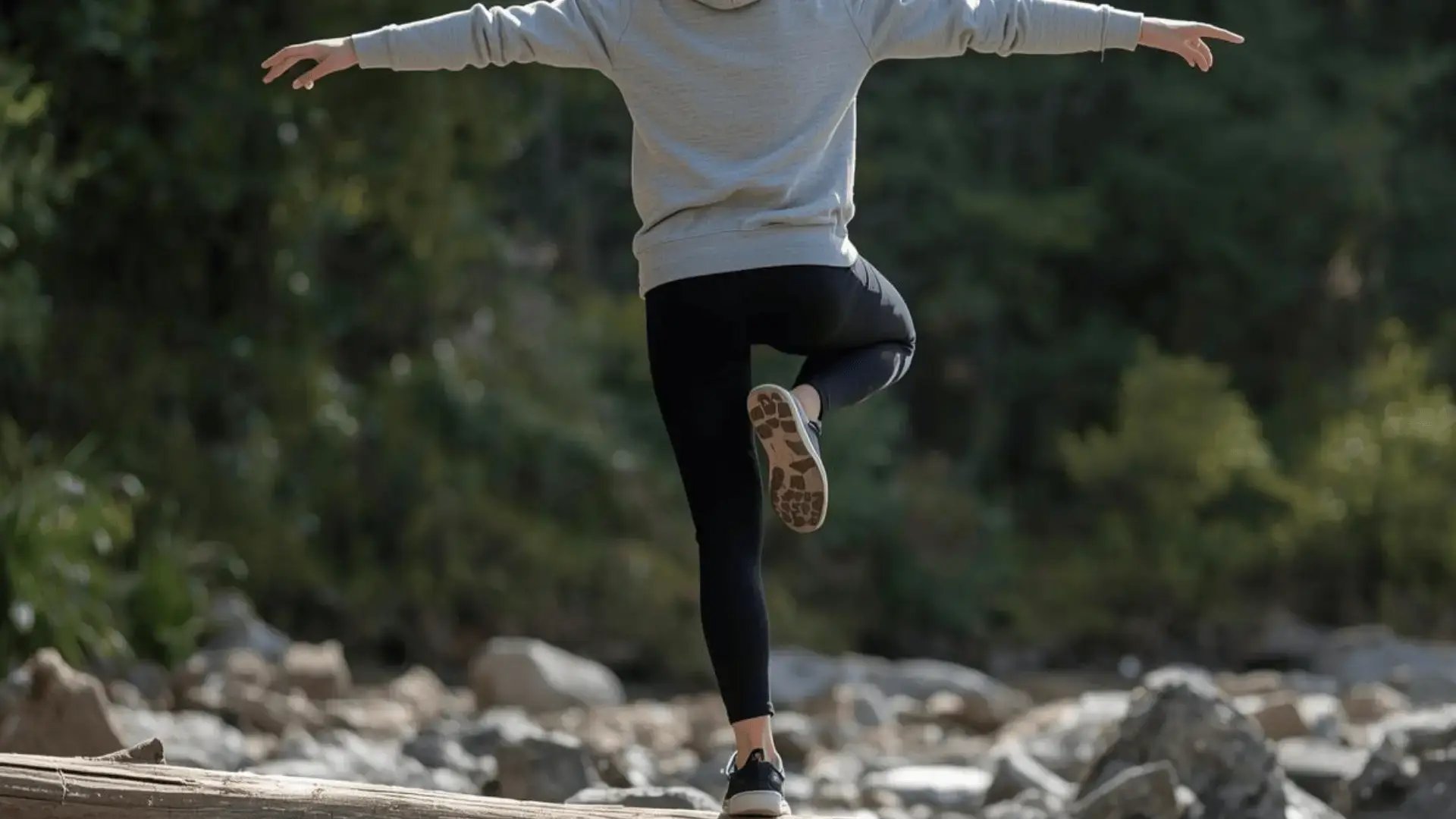 Person balancing on one foot on a log outdoors with arms outstretched, seen from behind in a rocky natural setting Trauma Therapist Institute