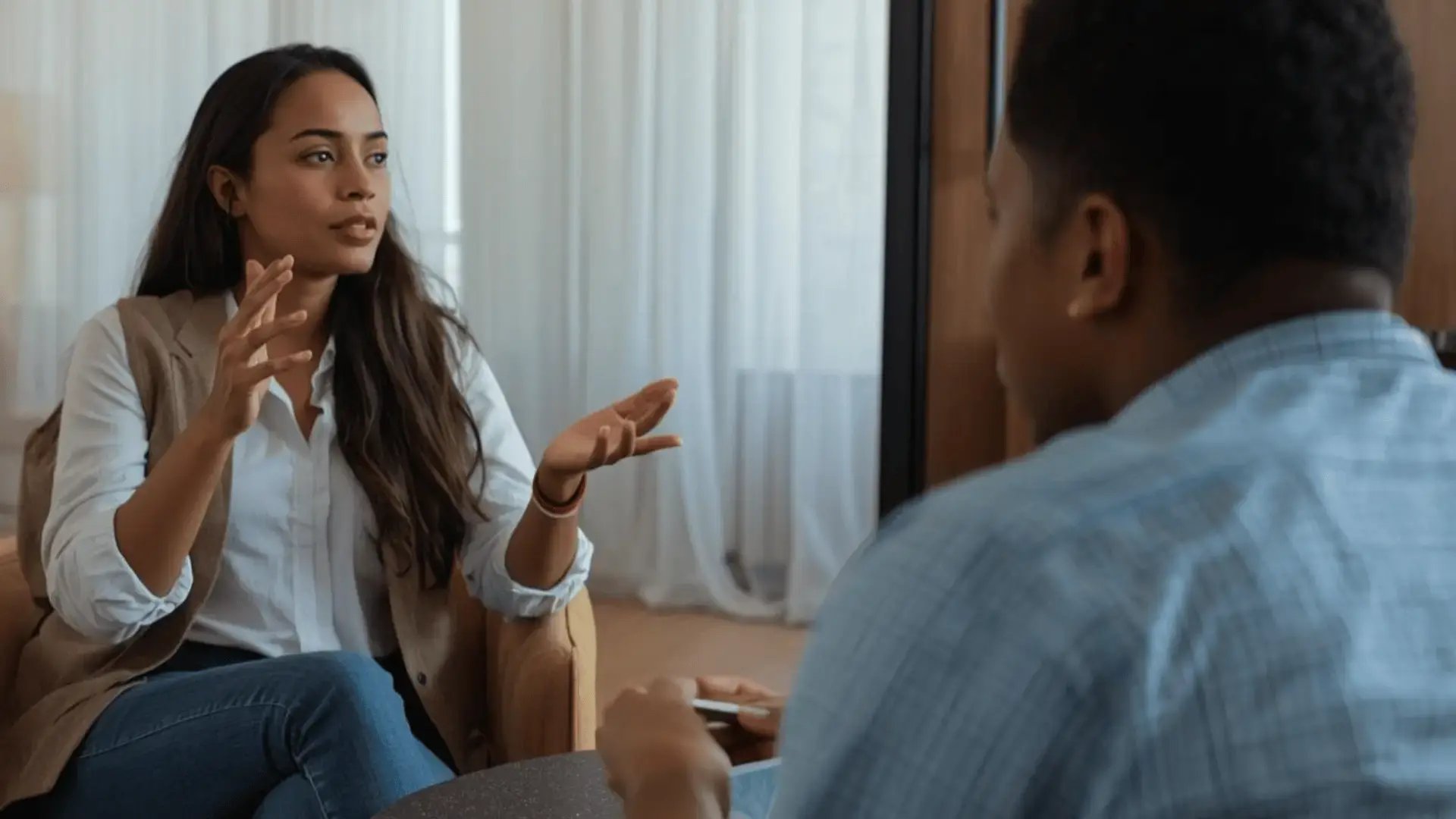 Therapist gesturing while explaining a concept to a client during a session in a warm, naturally lit room Trauma Therapist Institute