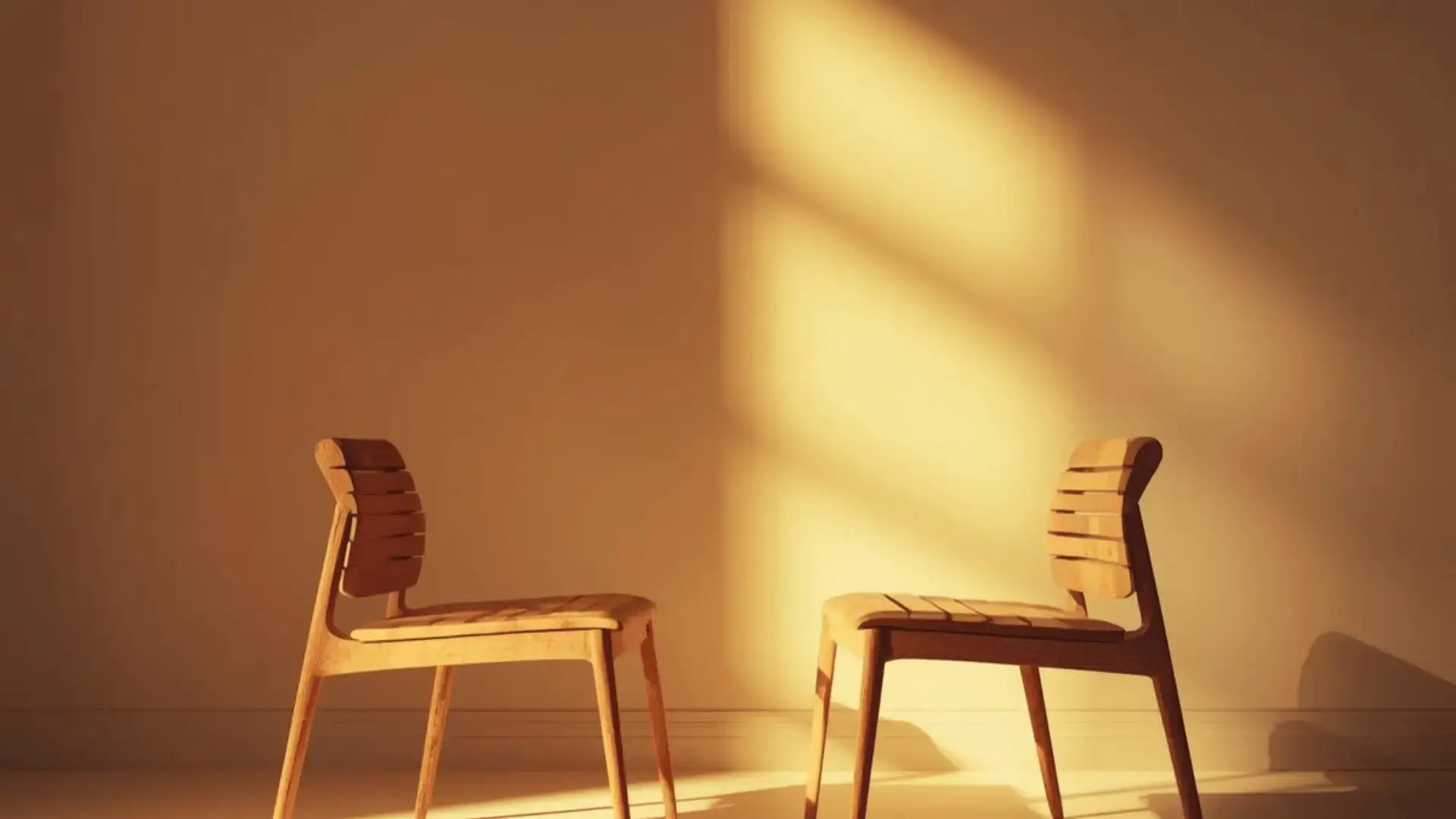 Two wooden chairs facing each other in a warm, sunlit room with soft light casting window shadows on the wall Trauma Therapist Institute